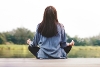 An image of a woman in the lotus yoga pose, facing away looking at a lake.