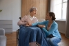 A young woman resting a blanket on a elderly woman in a wheelchair.