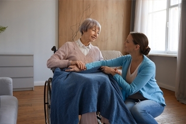 A young woman resting a blanket on a elderly woman in a wheelchair.